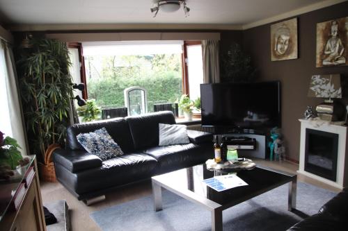 a living room with a black leather couch and a table at Veluwe Park Reewold Chalet Talisman in Putten