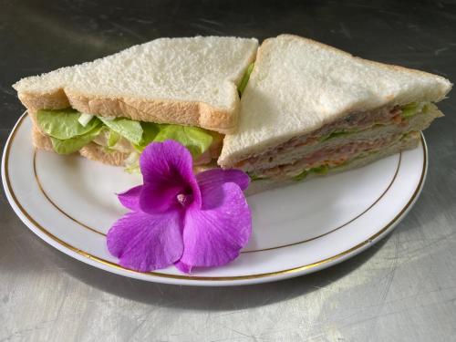 a sandwich cut in half with a purple flower on a plate at Khaosok Foresta Resort in Phanom
