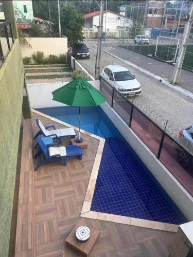 a swimming pool with a green umbrella and chairs and a table at Paraíso de porto in Porto De Galinhas