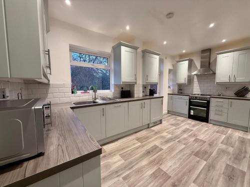 a large kitchen with white cabinets and wooden floors at Modern 5 Bed Home, TV in each room, Free BT WiFi & Parking - 62 BW in Solihull