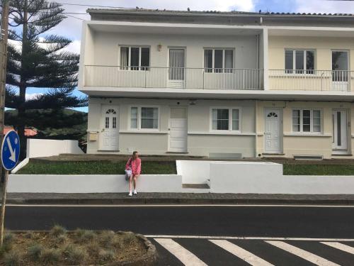 a woman sitting on a wall in front of a house at Casa dos Amigos in Angra do Heroísmo