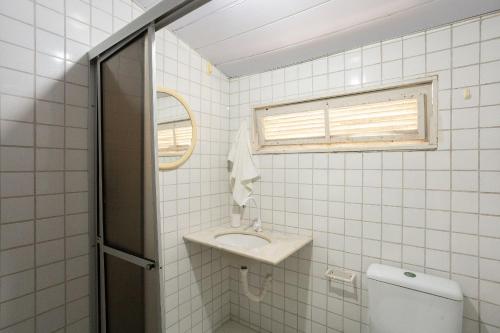 a white tiled bathroom with a sink and a toilet at Cohost Casa Pedra do Anel in Vila Velha