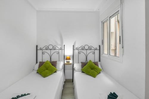 2 camas blancas con almohadas verdes en una habitación en Homely Apartments Las Salinas, en Torrevieja