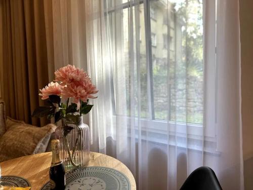 Un jarrón de flores sobre una mesa con una ventana. en Apartament Piastowska 2, en Polanica-Zdrój