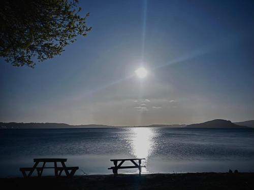 two picnic tables sitting in front of a body of water at Stillwater Residence - Lakeview Serenity Retreat in Ngongotaha
