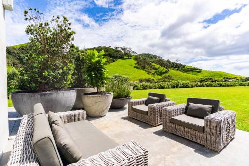 eine Terrasse mit Korbmöbeln und ein grüner Hügel in der Unterkunft Private Beach Access - Mangawhai in Mangawhai