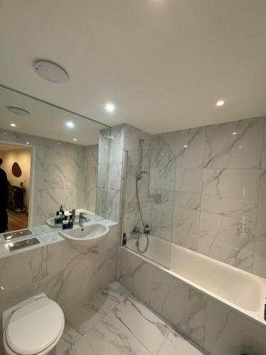 a bathroom with a toilet and a sink and a tub at Luxury flat with FREE parking & easy tube access! in London