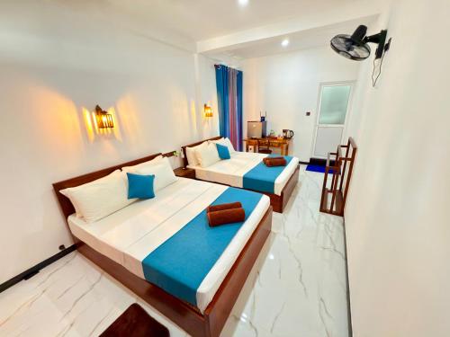 two beds in a hotel room with blue curtains at Devon Surf . Inn - Hiriketiya in Dickwella