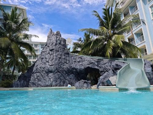 a pool in front of a resort with a rock formation at Grand Florida芭提雅带免费游泳池温泉桑拿浴和健身房瑜伽室私家海滩公寓E206 in Na Jomtien