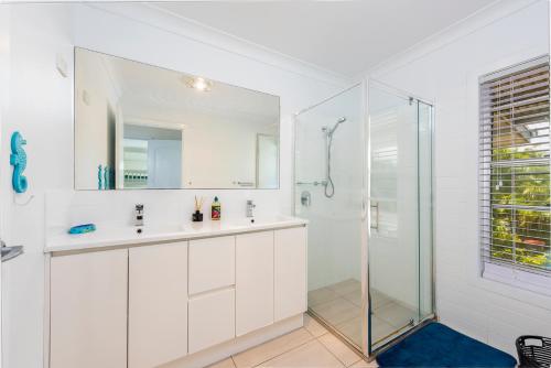 a white bathroom with a shower and a sink at Pet friendly beachfront home- sleeps 8 in Toogoom