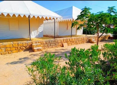 zwei weiße Zelte zwischen Bäumen und einer Steinmauer in der Unterkunft Jaisalmer Villa Resort & Camp Jaisalmer in Jaisalmer