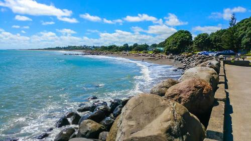 a beach with rocks and the ocean with people on it at Love It On Lemon - modern townhouse near CBD in New Plymouth