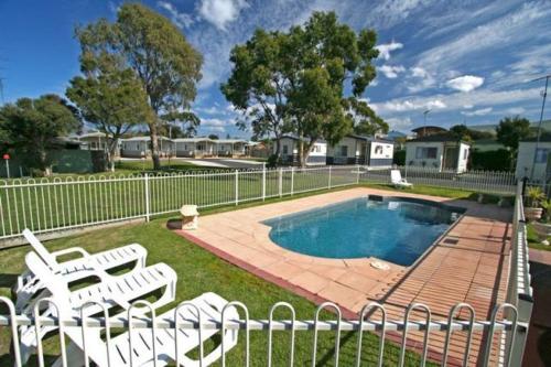 a fence with two white chairs and a swimming pool at Apollo Bay Holiday Park in Apollo Bay