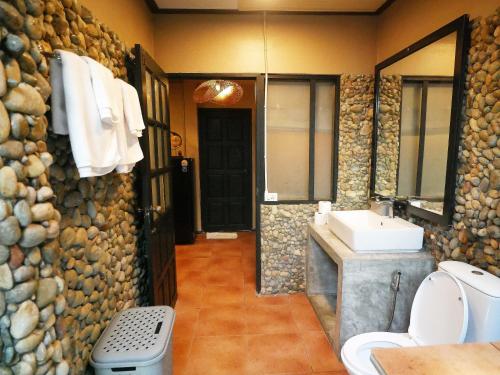 a bathroom with a stone wall with a sink and a toilet at Big Elk Steak House - HomeStay in Trat