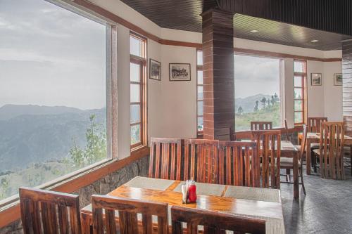 Un restaurante con mesas y sillas y grandes ventanales. en Echor - The Koti Village Resort Kufri, en Kūfrī