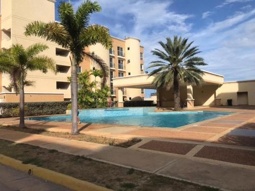 a swimming pool in front of a building with palm trees at Apartmento Minutos Caracola Beach in Porlamar