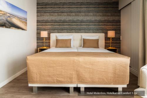 a bedroom with a large bed with two lamps at Hotel Molenbos Texel in De Cocksdorp