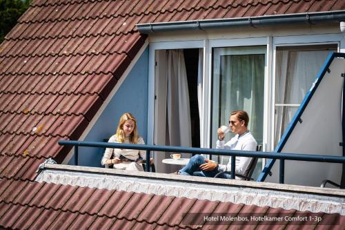 a man and a woman sitting on a balcony at Hotel Molenbos Texel in De Cocksdorp