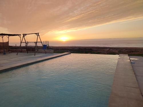 Una piscina con un columpio y la puesta de sol. en Tazgha house, en Essaouira