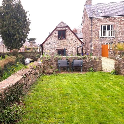 a stone house with two benches in a yard at Penybont Barn in Llangorse