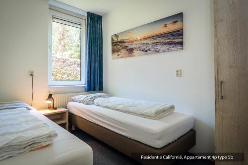 two beds in a room with a window at Residentie Californië in De Koog