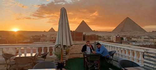 two men sitting at a table with an umbrella and the pyramids at Pyramids star of Khafre in Cairo
