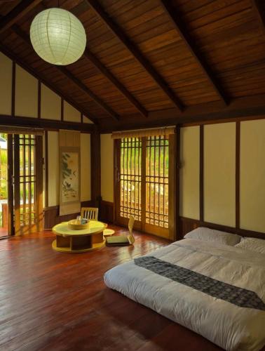 a bedroom with a bed and a table and windows at Aki house in Ban Bung Toei