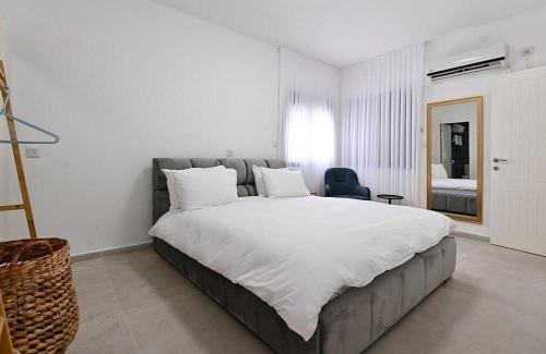 a bedroom with a large white bed and a chair at אחוזת סנטוריני - וילה מהממת עם בריכה מחוממת וג'קוזי בעין יעקב in ‘Ein Ya‘aqov