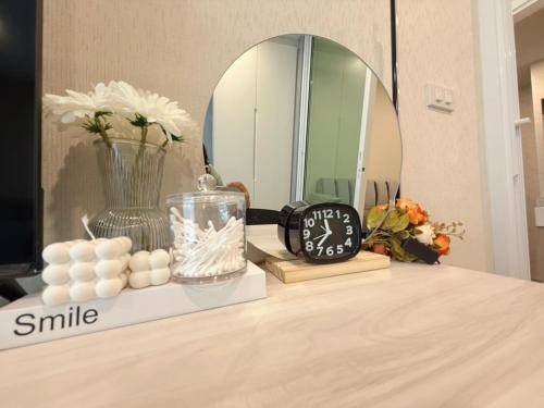 a table with a clock and a vase with white flowers at AVALYN Sweet Room - East Ville in Ban Hua Khao Sammuk