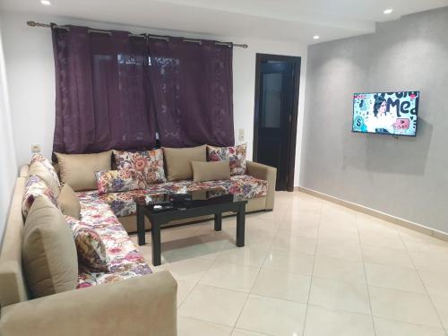 Una sala de estar con un sofá y un televisor en una pared. en Résidence EL AMAL, en Martil