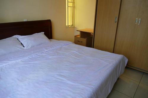 Un dormitorio con una cama blanca con cabecero de madera. en Home away from home, en Kigali