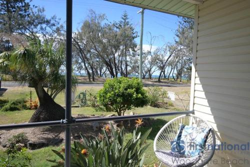 a porch with a wicker chair and a tree at 39 The Esplanade in Woodgate