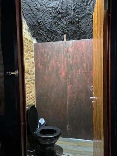 a bathroom with a black toilet and a wooden door at Hostel Fabulosa Casa de tijolinhos in Arapiraca