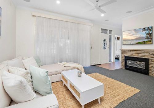 a living room with a white couch and a fireplace at Coastal Palms - Family & Pet-Friendly Beachside Haven in Lake Illawarra