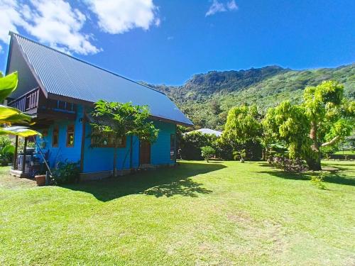 una casa azul con un jardín verde y montañas al fondo en Faré blue lagoon, en Moorea