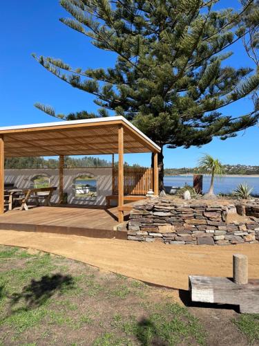 a wooden pavilion with a stone wall and a tree at Archy's on the Lake in Burrill Lake