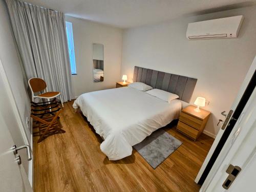 een slaapkamer met een wit bed, 2 tafels en een stoel bij Apartamento Sonho Terra in Ponta Delgada