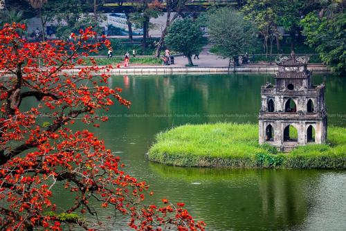 a building in the middle of a pond with red flowers at Nhà nghỉ Minh Quảng in Hanoi