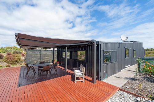 a tiny house with a deck with a table and chairs at Lighthouse-hideaway in Cape Foulwind