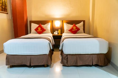 two beds in a hotel room with red pillows at Nueve Malioboro Hotel Yogyakarta in Yogyakarta