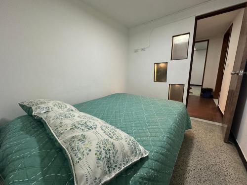 a bedroom with a bed with a green comforter and a pillow at Apartamentos FM 204 in Líbano