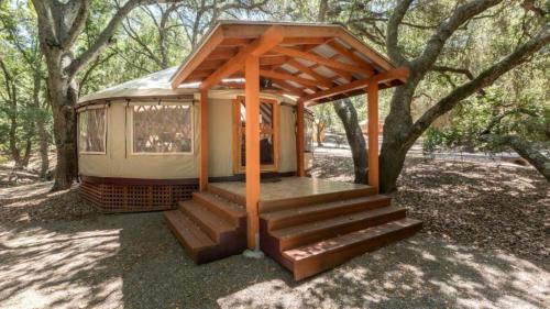 Una pequeña casa con porche y escaleras en un bosque. en Elegant Yurt Tucked Beneath Oak Trees on Southern California Ranch, en Cayucos