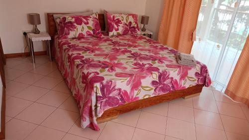 a bedroom with a bed with a pink floral bedspread at Skyline View Garden Apartment in Bel Ombre
