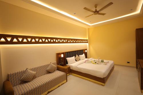 een slaapkamer met een bed, een bank en een plafondventilator bij Ramaya Motel & Resort, Ujjain in Ujjain