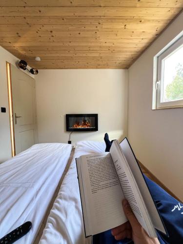 a person reading a book on a bed with a fireplace at Nature&Chill Treehouses in Sopron