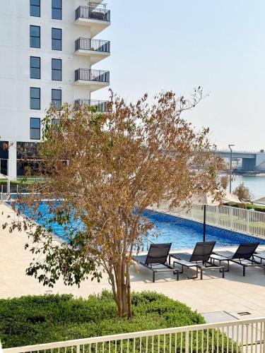 a tree and chairs next to a swimming pool at Chic Yas Stay, F1, Ferrari, Sea World Yas Island in Abu Dhabi