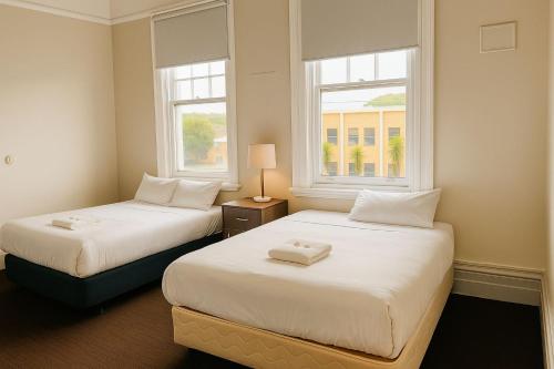 twee bedden in een kleine kamer met twee ramen bij Leura Hotel in Camperdown