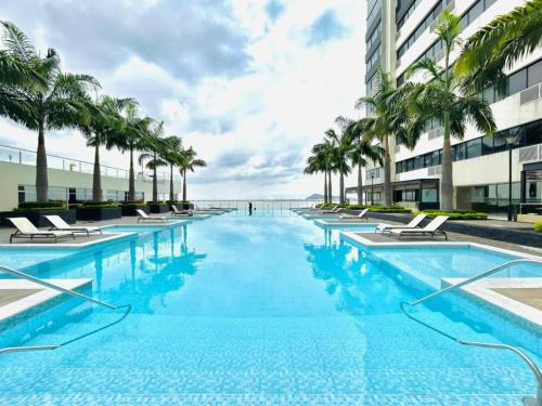 une grande piscine avec des palmiers et un bâtiment dans l'établissement Bellini, Hermoso Departamento y 1 Plaza de Parqueo Gratis, à Guayaquil