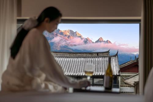 a woman sitting in front of a window with a mountain view at 37 Courtyard（Baisha Ancient Town） in Baisha