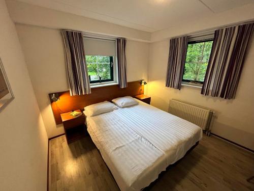 a bedroom with a white bed and two windows at Esdorp Bungalow | 6 personen in Hooghalen